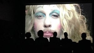 Silhouetted audience watch a transvestite on screen