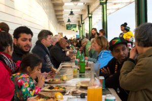 Long table of people of all ages enjoying a community meal.