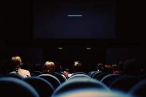 There are people in a cinema looking towards the screen which is not on.