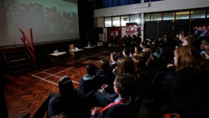 A school hall full of children watching a film onscreen.