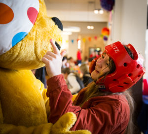 A young person wearing a protective helmet touching the head of a person in a bear costume.