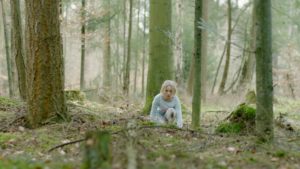 Still from the film System Crasher of a young person crouching in the woods.