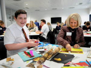 An older person and a younger person smiling doing crafts at a table.