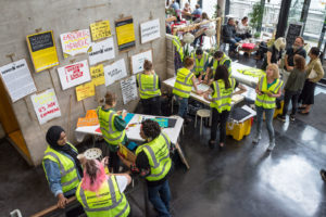 A group of female identifying people of different ages wearing hi-vis vests making and displaying banners