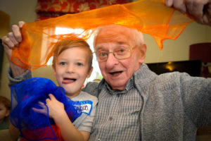 Older person with a young person looking happy holding a piece of orange coloured gauze above their heads.