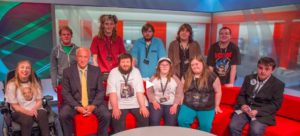 Group of neurodivergent and disabled people lined up along and behind a sofa in BBC Newcastle studio.