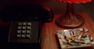 Still of black telephone next to the base of a lamp and an ashtray filled with cigarette butts