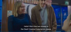 Two people at a box office with subtitles which say: "Hello! We'd like two tickets for the Deaf Cinema Experience please"
