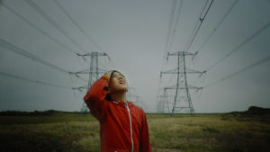 Boy in red jacket looks up at pylons and electrical lines