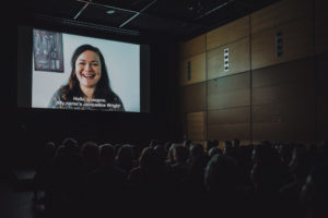 Cinema screen with subtitled film and audience in the dark.