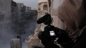 Still from documentary film For Sama of a woman looking over a syrian war zone with a film camera