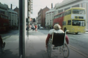 Archive film footage from the 80's show a wheelchair user going along the street