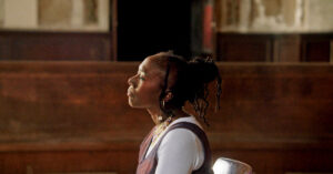 Black woman in profile sits mid-frame in a room - Still from 13th by Ava Duvernay
