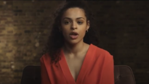 Screenshot of a video. A person in red speaking to the camera
