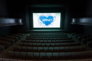 Dark cinema with lit up white screen with a blue heart logo which says "MIND"