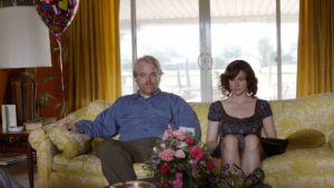 Still from the film Savages of two middle aged people sitting on a sofa.