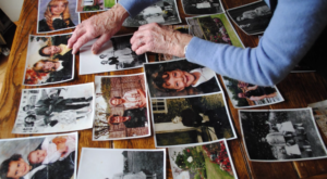 An older person's hand arranges family photos on a desk.