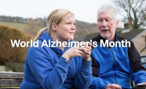Screenshot from Alzheimer's Society website. A woman and an older man sit on a bench outside drinking from a flask. Text overlay says: World Alzheimer's Month