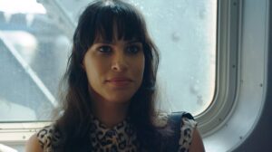 Still from the film Appropriate Behaviour. A women (Desiree Akhavan) with long dark hair wearing a leopard print sleeveless top stands facing the camera, a window is behind her.