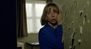 Sally Hawkins clutches a wall covered in torn wallpaper, and looks fearful, in 'Eternal Beauty'