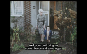 A very small woman walks out of a house with an average height woman. they are wearing 70s attire, pattered clothes, and walk up a garden path. The captions reads 'Well you could bring me some bacon and some eggs.'