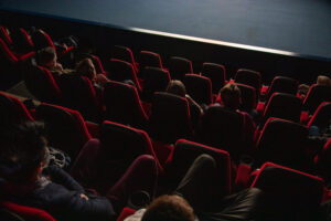 View of an from above. The seats are read and they are watching a film, the light from the screen makes the audience and stage visible.