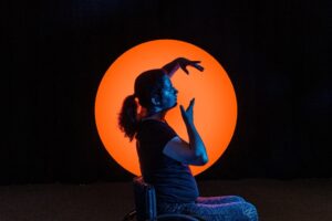 Photo oof a person sitting dancing against a bright orange light on a black background